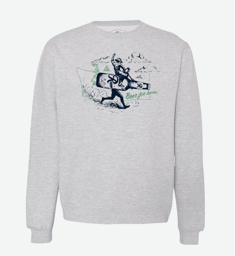 Heather grey crewneck sweatshirt by The Great PNW featuring a vintage graphic of a cowboy riding a giant running Rainier Beer bottle. The design includes a light green outline of Washington state in the background and the text "Beer for here." written in green cursive.